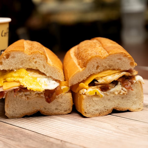 Two deli breakfast sandwiches with fried eggs, cheese, and bacon on a wooden table.