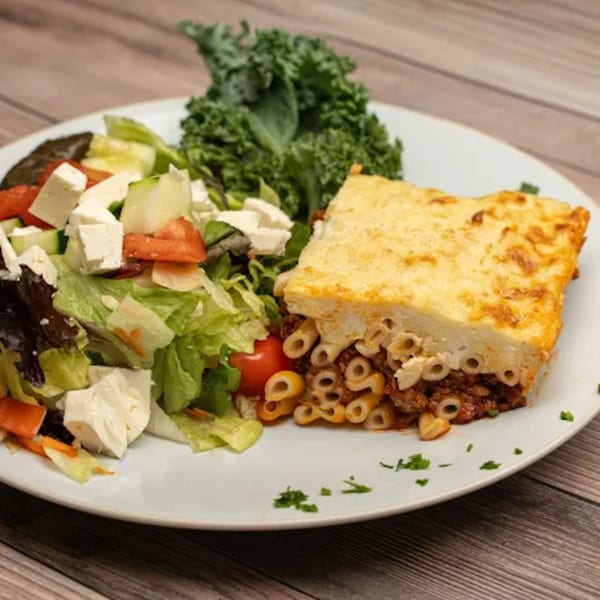 Pastitsio with a side salad topped with feta cheese and tomatoes, and a garnish of kale.