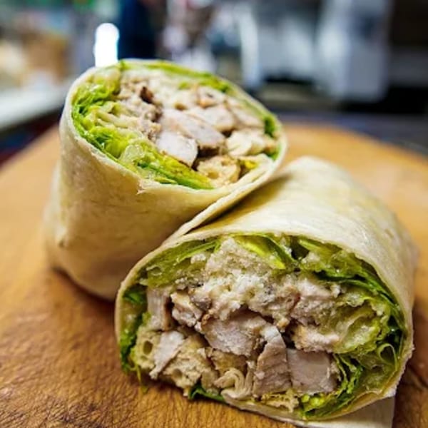 Two halves of a deli chicken Caesar wrap, filled with lettuce, chicken, and cheese.