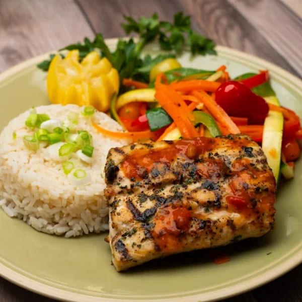 Grilled fish with sauce, white rice, and colorful sautéed vegetables on a light green plate.