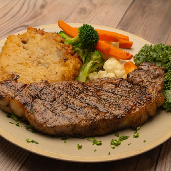 Grilled steak with a side of golden-brown potato pancake, steamed carrots, broccoli, and cauliflower.