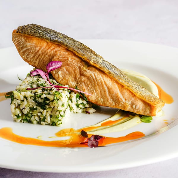 Pan-seared salmon with crispy skin, served atop herbed rice, garnished with microgreens and sauces.