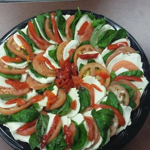 A platter of Harry's Hilltop Caprese salad with sliced tomatoes, mozzarella, basil, and roasted red peppers.